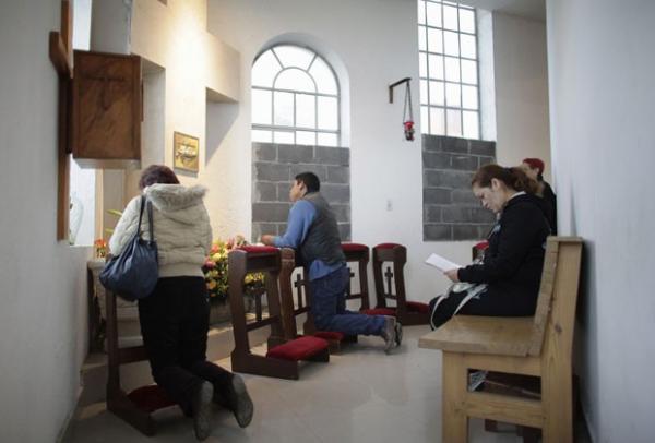 Católicos rezam perto de janelas cobertas parcialmente com blocos de cimento no interior da igreja de Santa Teresa de Ávila em Monterrey(Imagem:Reprodução)